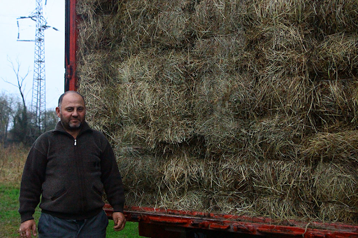 A man stands next to a large container full of bales of hay.