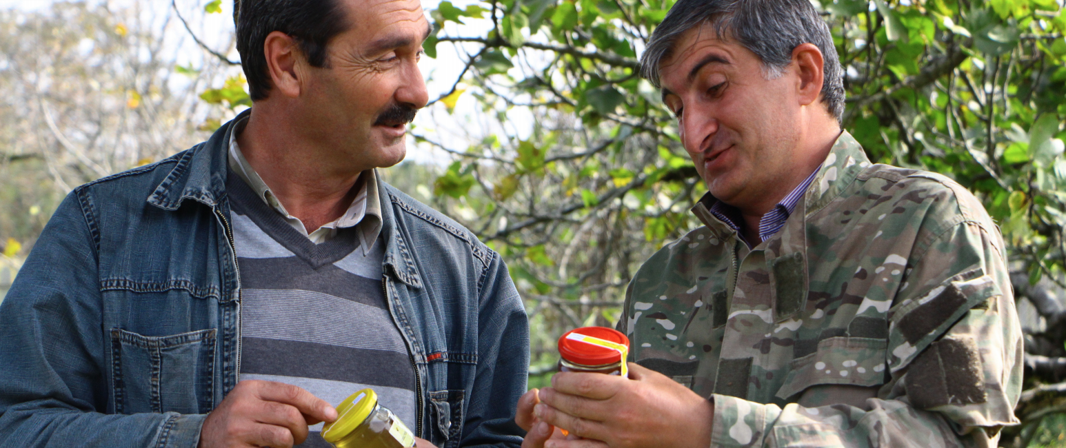 Two men look at honey in glass jars.